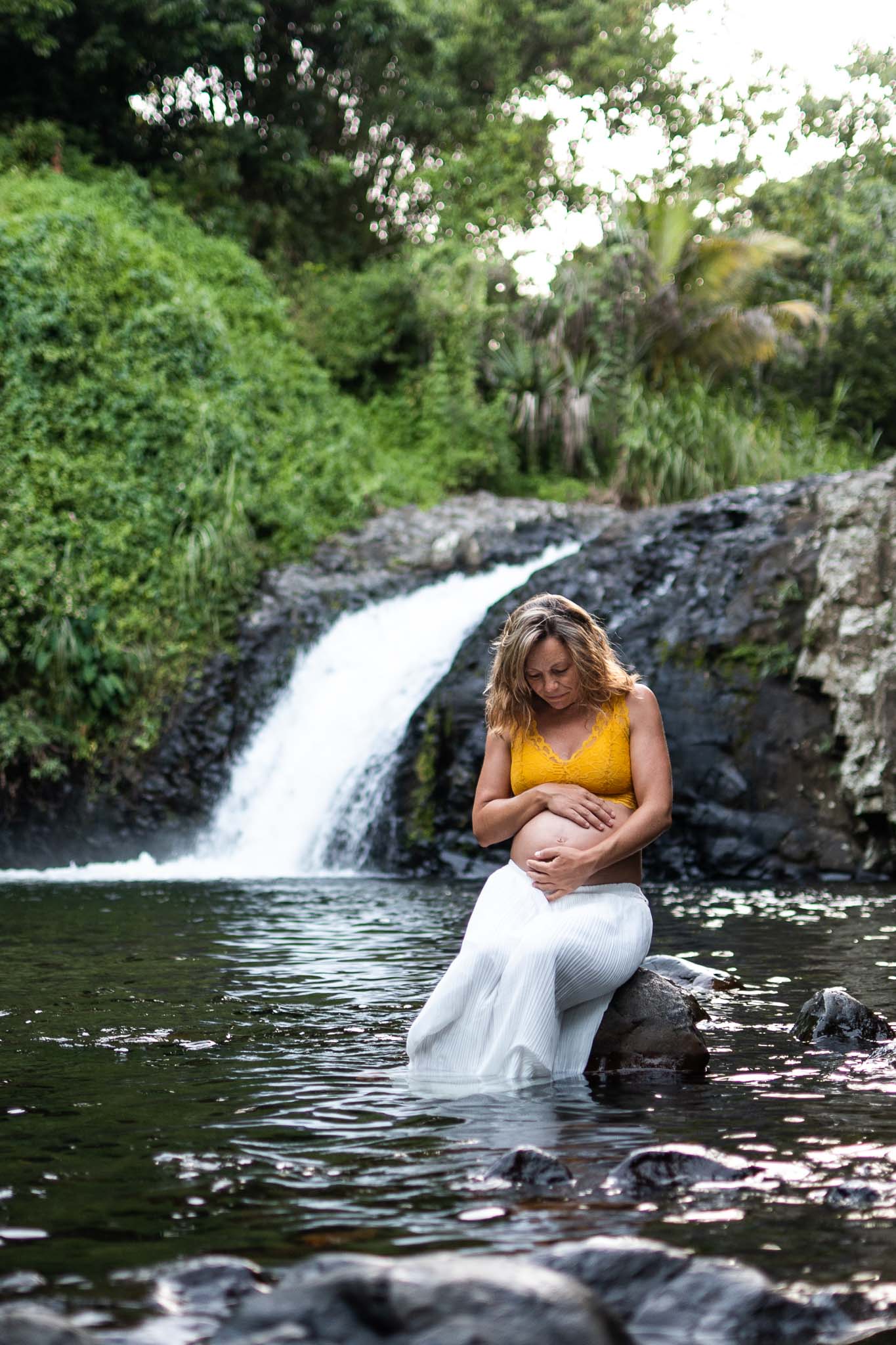 femme assise au bord d'une cascade. Elle regarde son ventre